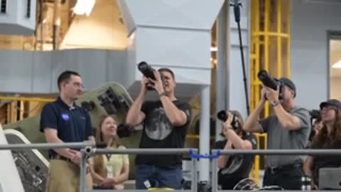 Astronauts hold large camera lenses up toward the ceiling.