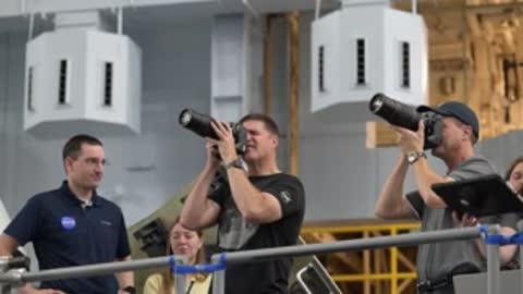 Two astronauts practice holding and aiming large camera lenses.