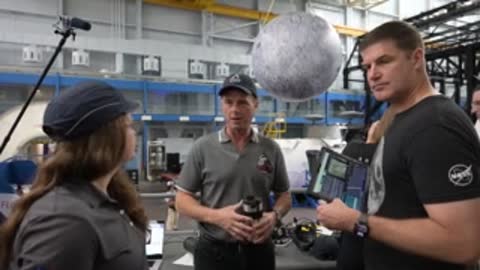 Astronauts converse near a simulator and hanging moon model.