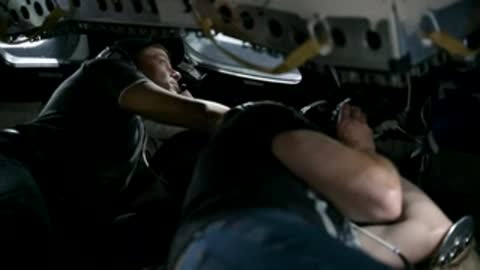 An astronaut rests inside a darkened spacecraft simulator cockpit.