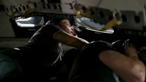 Astronauts in vehicle training simulation, adjusting controls.
