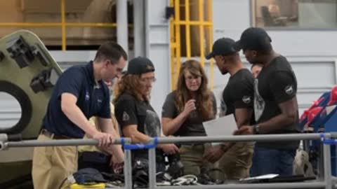 Group of instructors and astronauts gathered around documents on a railing.