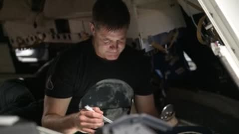 Astronaut in black shirt writing at desk during simulation.