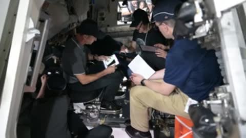 Astronauts seated together in simulator reviewing documents.