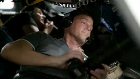 Astronaut in grey shirt holding camera inside vehicle.