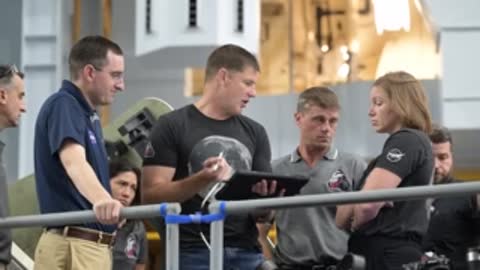 Astronauts standing by railing discussing notes outdoors.