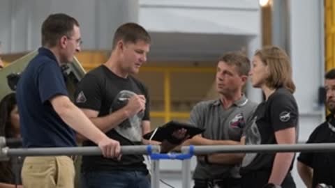 Astronauts conversing near railing in training facility.