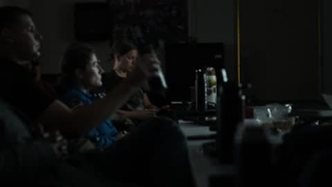 People seated in dimly lit mission control watching screens.
