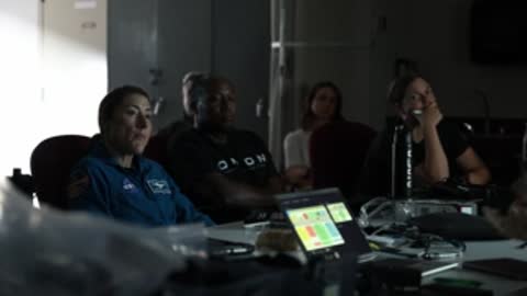 Astronauts seated in briefing room watching presentation.