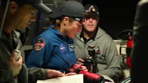 Astronauts examining camera equipment in simulator cockpit.