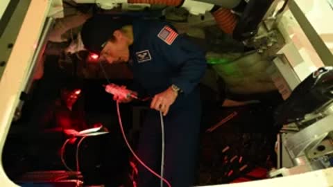 astronaut working inside a spacecraft cabin with red lighting and equipment, medium shot.
