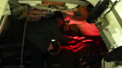astronaut working in a dimly lit spacecraft cabin with red instrument lights, medium shot.