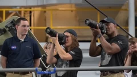 Instructors and astronauts practicing holding and aiming large camera lenses.