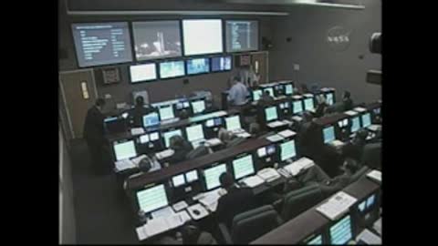 Static wide shot of a NASA mission control room filled with working staff.