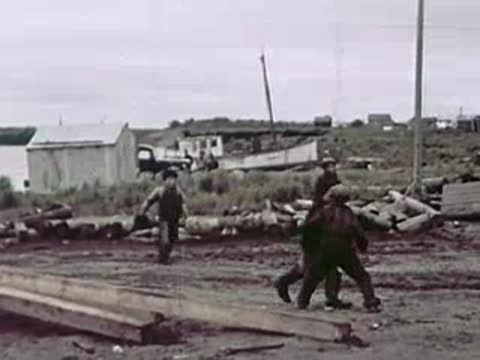 Men working outdoors near stacked logs and wooden beams.