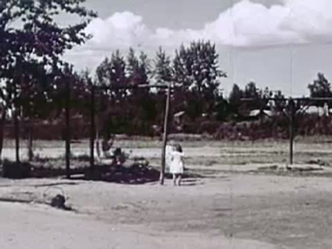 Two children standing outdoors near trees and a fence.