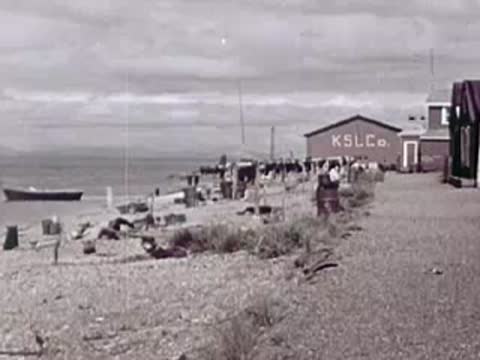 Coastal village with small buildings, boats, and racks on a gravel beach