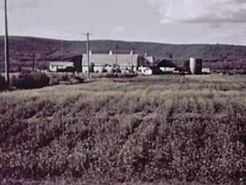 Rural farm scene with buildings, hills, and a field in the foreground