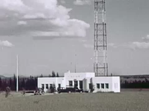 A modern white building with a tall communications tower stands in a flat grassy area.