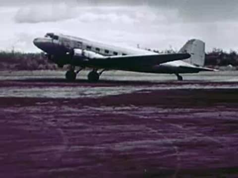A twin-engine airplane taxis on an airfield with a cloudy sky overhead.