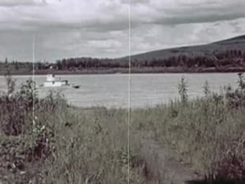 Small boat cruising on a wide river with grassy banks and distant hills