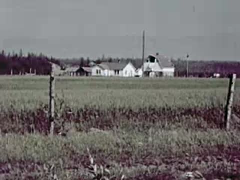 Rural landscape with a wooden fence and distant farmhouses under an overcast sky