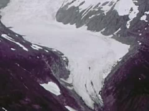 A massive glacier flowing through a snow-covered mountain valley, aerial view, 1940s
