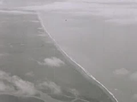 Aerial view of a long coastline with beaches and distant clouds, 1940s