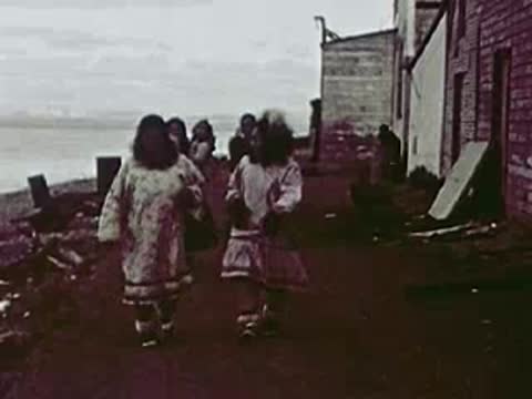 People walking along a coastal path near wooden buildings, Alaska, 1940s