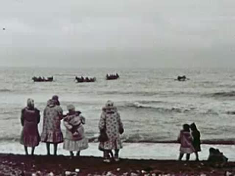 Group of people standing on a beach watching boats on the water, 1940s