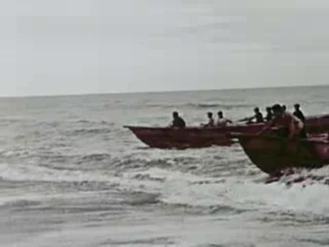 A boat approaching the shore with people wading in the surf, 1940s