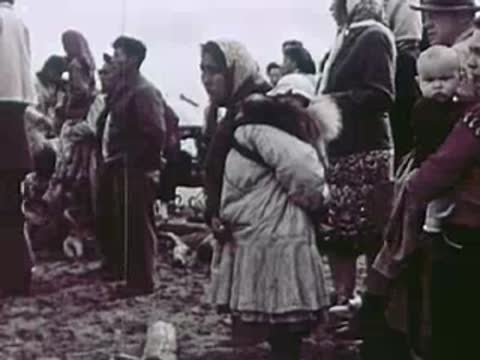 An Indigenous woman carrying a baby in her parka outdoors.