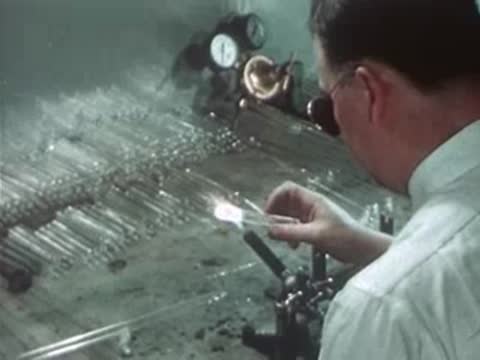 Worker heating and shaping a glass tube with a torch.