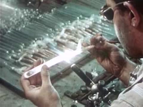 Close-up of a worker carefully shaping a glowing glass tube.