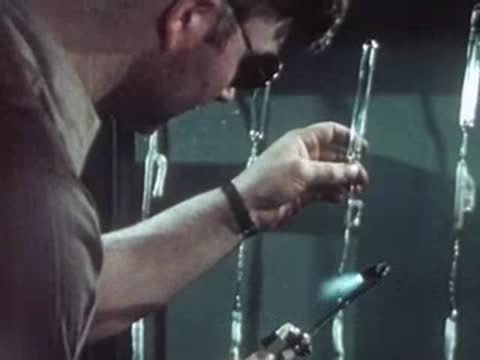 Technician vertically processing quartz glass tubes with a flame torch.