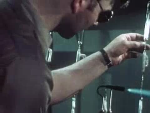 Worker moving a flame torch near vertical glass tubes in the lab.