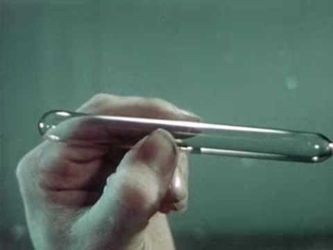 Close-up of a finished glass capsule being inspected by a worker.