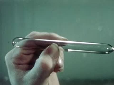 Worker holding and inspecting a sealed glass capsule in a workspace.