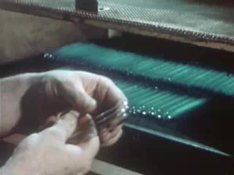Factory worker sorting and placing glass tubes into designated slots.