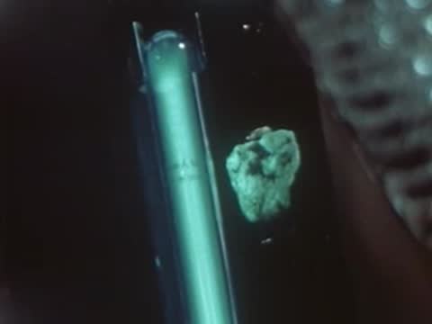 Macro view of glowing green fluorescent mineral sample under ultraviolet lamp.