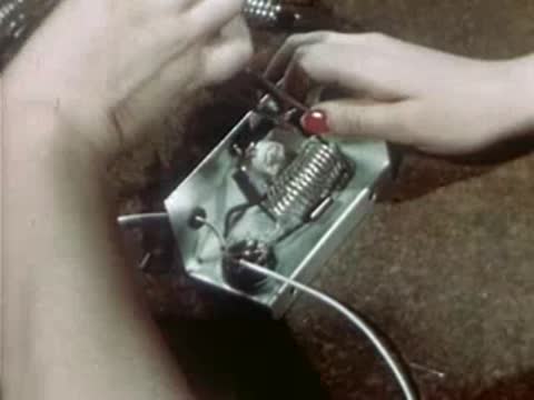Worker assembling electrical wiring inside metal casing at factory workbench.