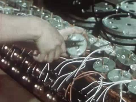 Multiple workers assembling electrical devices on long factory production line.