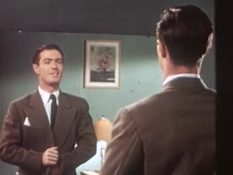 Dapper man in suit adjusting tie and looking in mirror.