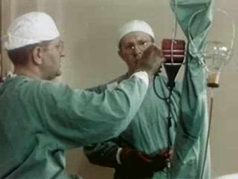 Surgeon adjusting medical equipment next to another doctor in an operating room.