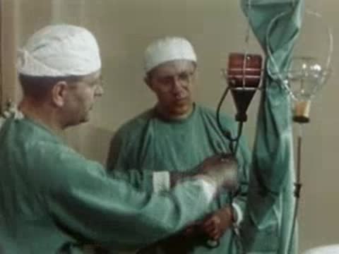 Surgeon adjusting tubes on a medical device with an assistant watching.
