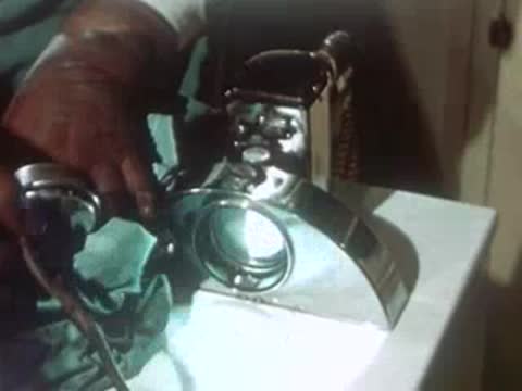 Hands turning on a specialized chrome medical lamp on a stand.