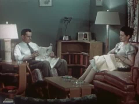 Couple sitting in a living room, man reading newspaper, 1940s style.