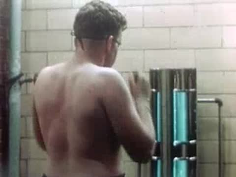 A shirtless man stands in front of a vertical ultraviolet therapy lamp in a clinic.