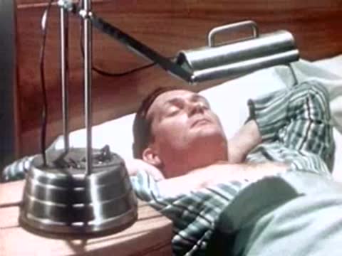 A man lies in bed with protective goggles while an ultraviolet lamp shines above him.