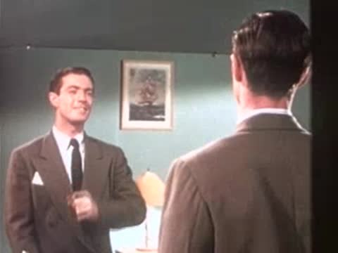 A well-dressed man in a suit looks at his reflection in a mirror.